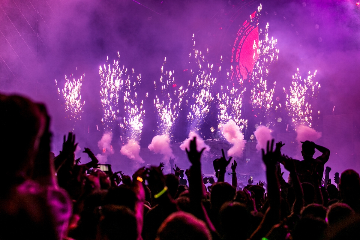 Creating a VIP Catering Experience at Summer Music Festivals 1 A crowd at one of the vibrant summer music festivals watches a concert with hands raised as fireworks and smoke effects light up the stage in purple and pink hues.