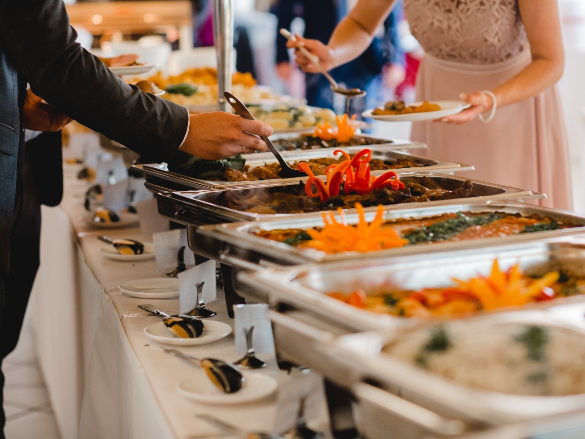 Back to School Dinner Ideas for Educational Events 9 People serving themselves food from a buffet table with trays of various dishes and decorative garnishes—a perfect setup for back to school dinner ideas. Plates, spoons, and name cards are neatly arranged along the table.