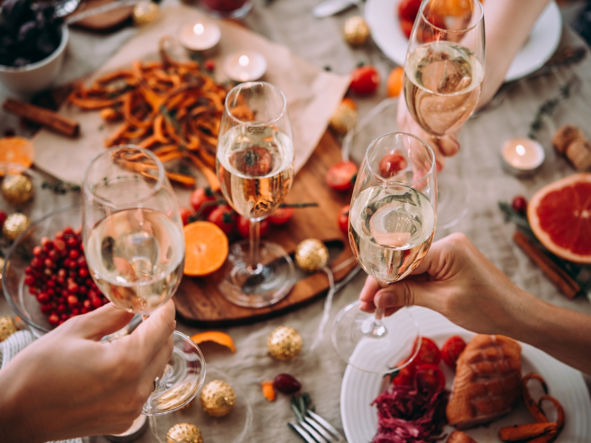 Blending Autumn Flavors Into Your Corporate Catering Menus 6 Four people clink glasses of sparkling wine over a festive table set with food, candles, fruit, and holiday decorations, showcasing the elegance possible with expertly curated corporate catering menus.