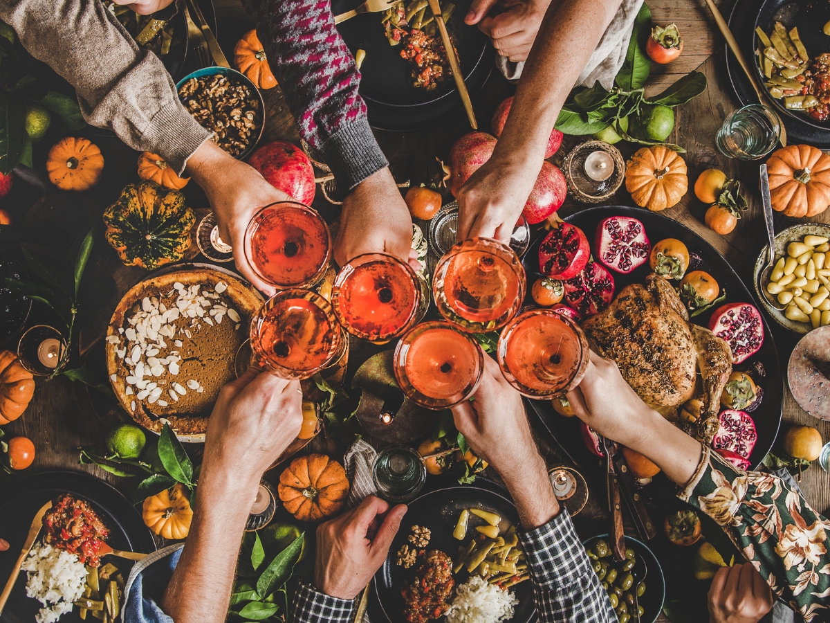 Catering Blog 1 Several people raise glasses for a toast over a festive table filled with various foods, fruits, small pumpkins, autumn-themed dishes, and delights inspired by corporate catering menus.