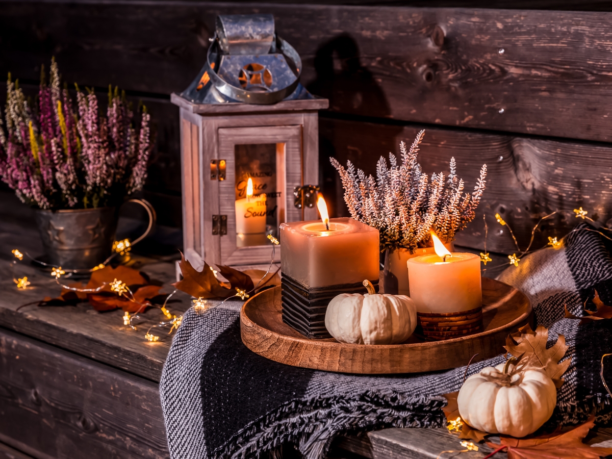 Planning a Fall-Themed Wedding Reception Menu: Seasonal Delights for Your Big Day 8 A wooden tray with two lit candles, small white pumpkins, and sprigs of lavender sits on a checkered blanket, beside a lantern and a vase of flowers, with string lights adding charm to this Fall-Themed Wedding Reception scene.