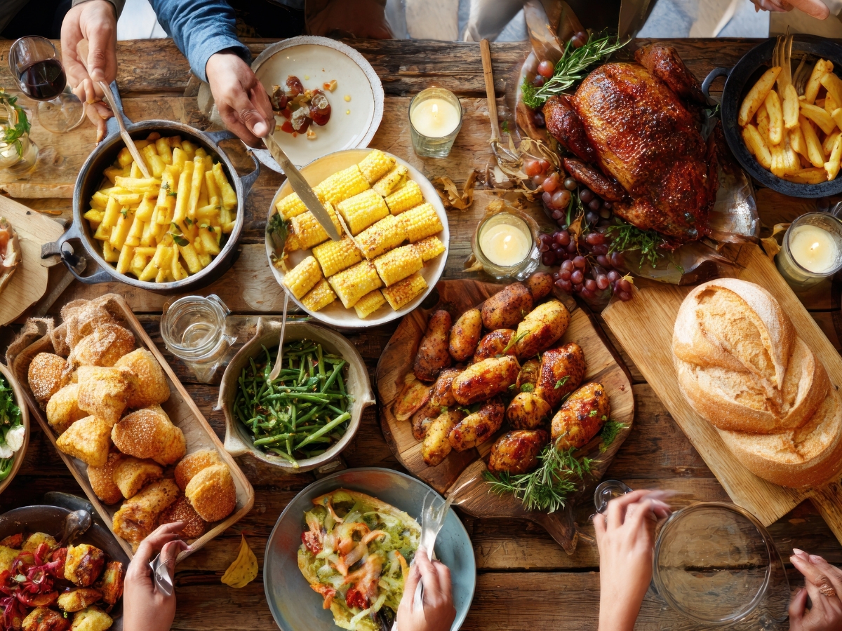 Unique Thanksgiving Catering Menu Ideas to Impress Your Guests 5 A table set with roast chicken, corn on the cob, green beans, bread, salad, potato wedges, pasta, and people serving food from a delicious Thanksgiving Catering Menu.