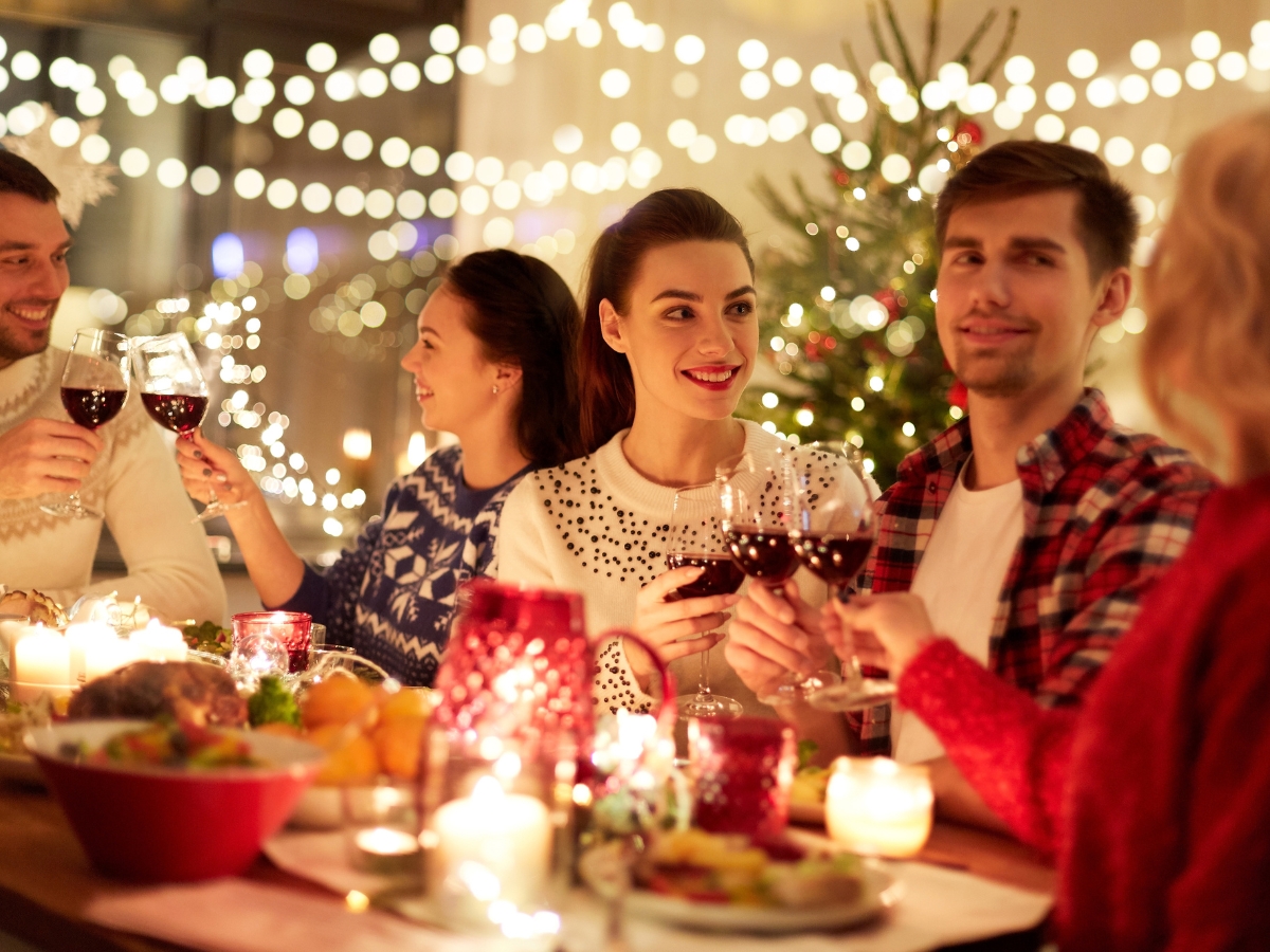 Christmas Party Catering Ideas for Intimate Gatherings 1 Five people sit around a decorated table, clinking wine glasses beneath festive lights and a Christmas tree—perfect inspiration for your next gathering or to explore new Christmas Party Catering Ideas.