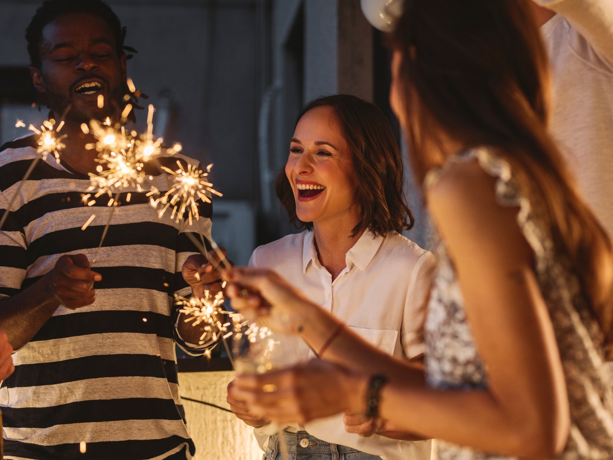 New Year's Eve Catering Tips: Create a Memorable Celebration 3 Three people hold lit sparklers and smile while standing together at an indoor New Year's Eve Catering gathering.