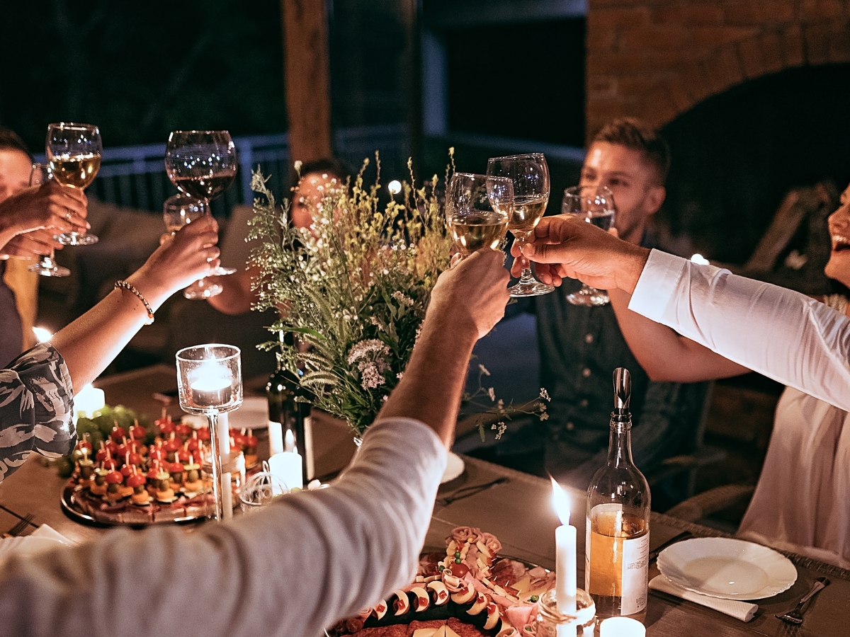 A group of people seated at a candlelit table raise their glasses in a toast, celebrating successful corporate team building, surrounded by food, candles, and a beautiful flower arrangement.