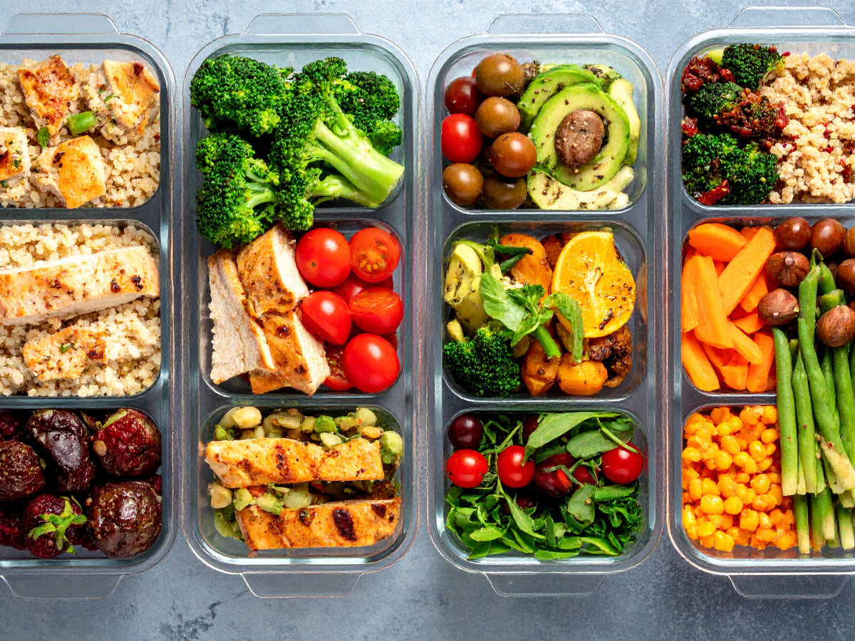 Three meal prep containers filled with assorted vegetarian foods including grilled vegetables, quinoa, tomatoes, avocado, corn, green beans, and mushrooms, all arranged neatly in compartments.
