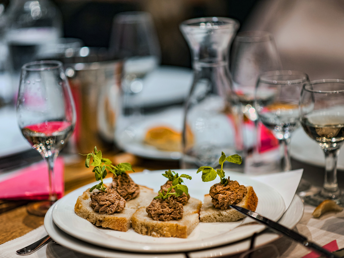 Cocktail Pairing Tips for Better Food and Drink Matches 5 Four slices of bread topped with a brown spread and greens are arranged on a white plate; wine glasses and a water carafe in the background hint at an elegant cocktail pairing.