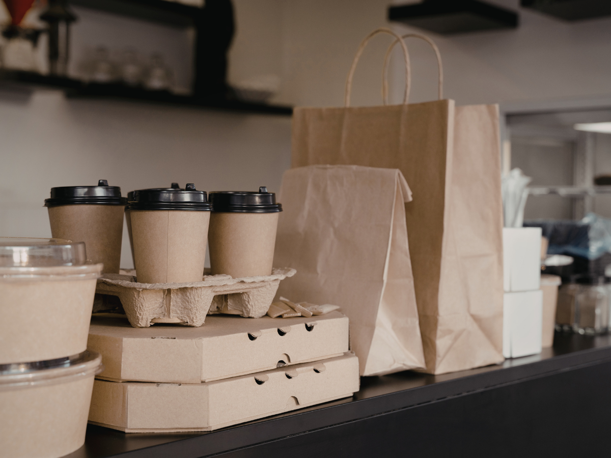Eco-Friendly Packaging Ideas for Modern Catering 3 Takeaway coffee cups, food containers, and brown paper bags made from eco-friendly packaging are arranged on a counter, suggesting a cafe or restaurant setting prepared for food delivery or takeout orders.
