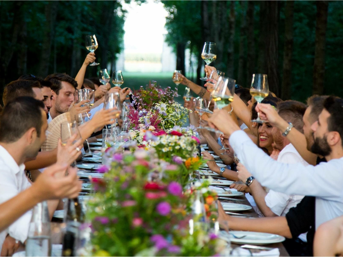 Charming Rehearsal Dinner Catering in Metro Atlanta: Personalized Wedding Catering Solutions 1 A group of people sitting at a long outdoor table, raising glasses in a toast, with flowers arranged in the center—an unforgettable scene enhanced by elegant rehearsal dinner catering.