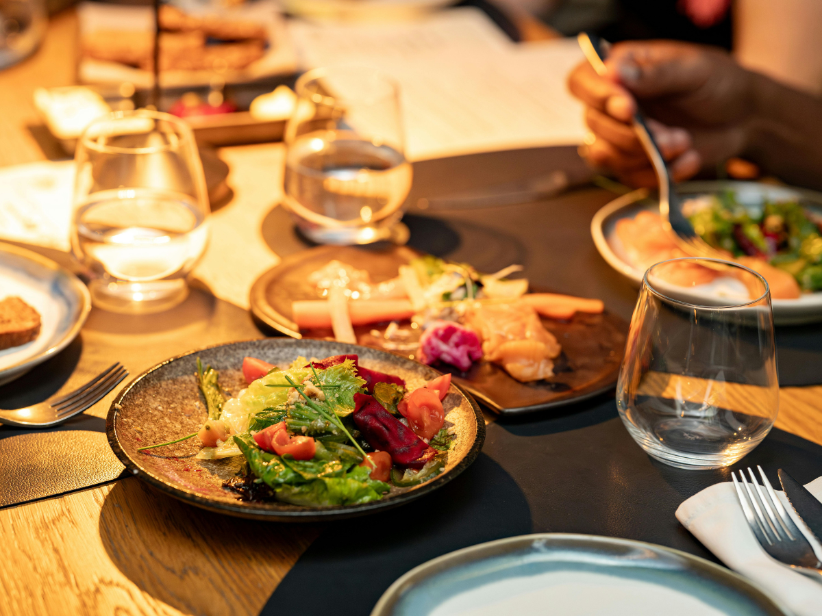Charming Rehearsal Dinner Catering in Metro Atlanta: Personalized Wedding Catering Solutions 2 A dinner table set with glasses of water, salads, smoked salmon, and cutlery creates an inviting scene—perfect for rehearsal dinner catering—with a person holding a fork near their plate.