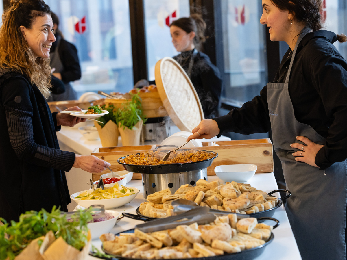 A woman in a grey apron serves a dish from a large pan at an event rentals Atlanta buffet.